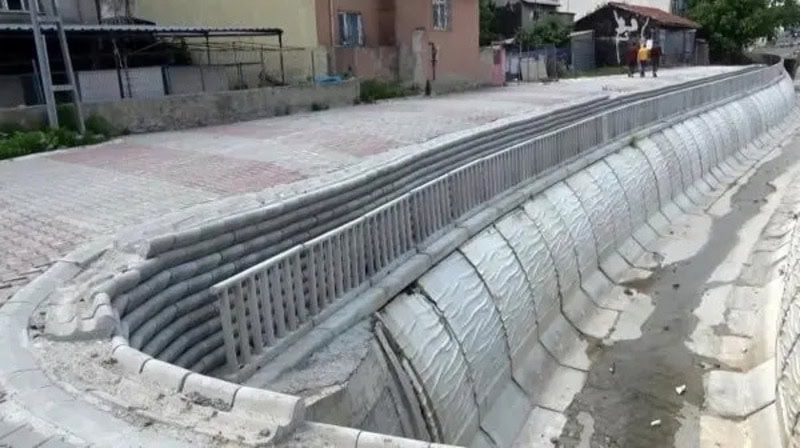Damaged sidewalk with exposed pipes and broken concrete in a dangerous design.