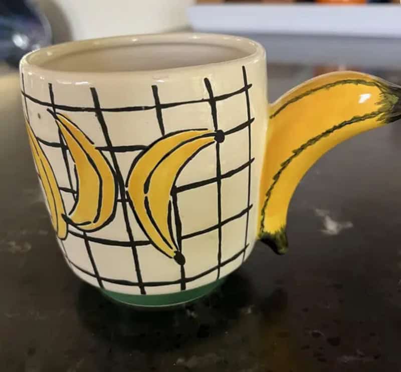 Mug with banana and grid design, handle shaped like a banana, on a black surface.