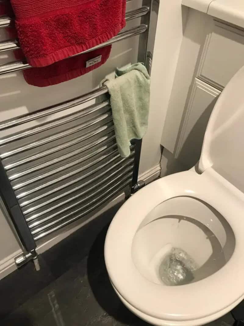 Toilet next to a heated towel rail with towels hanging on it.