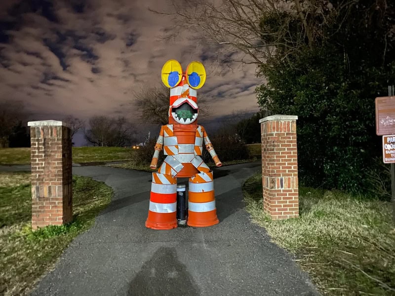 Colorful, large cartoonish creature sculpture at night near brick pillars.