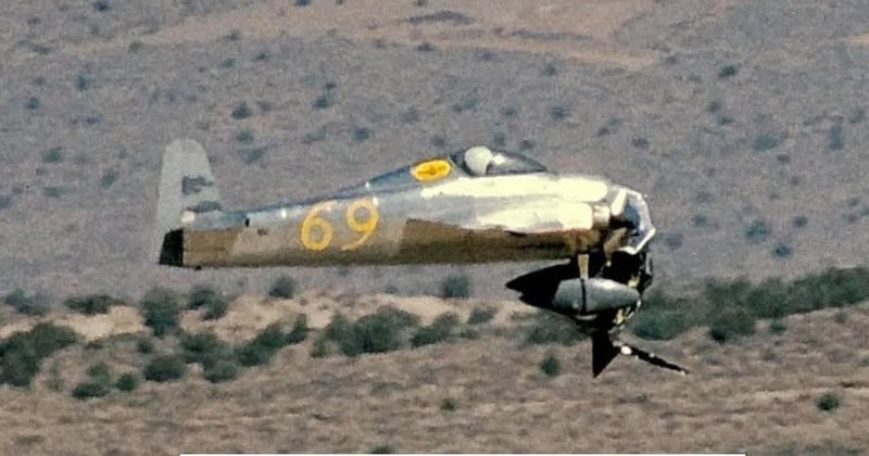 A military jet with the number 69 flying low over desert terrain.