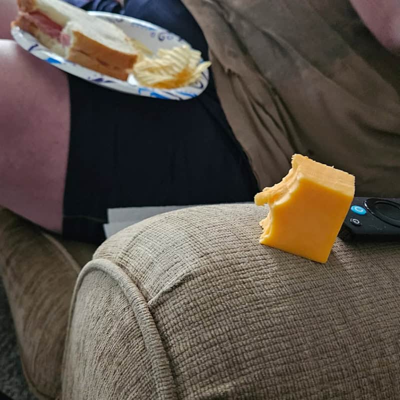 Cheese on the armrest with a plate of food and a remote nearby.