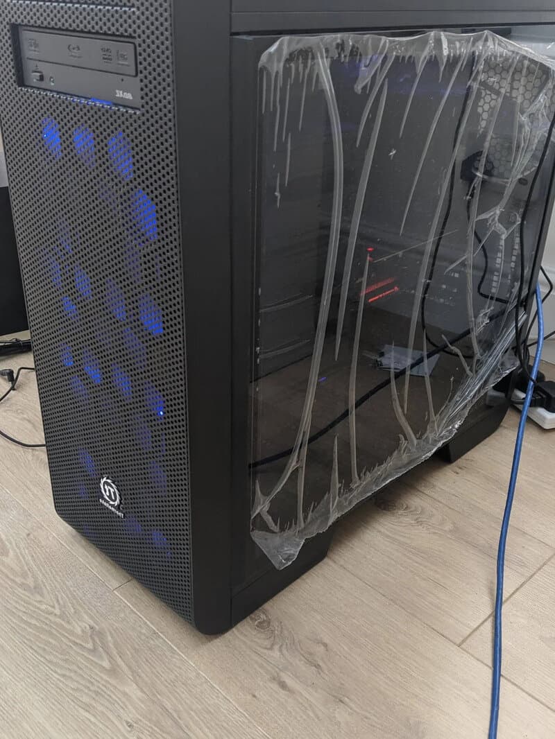 Computer tower with plastic wrap on the side, blue LED lights, and cables connected.