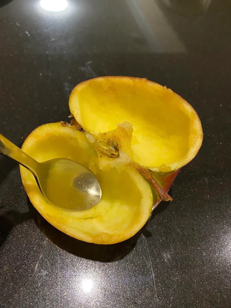 Half-eaten yellow apple with a spoon inside, on a black surface.